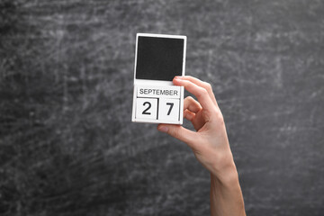 Wooden block calendar with date september 27 in female hand on background of school chalk blackboard