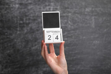 Wooden block calendar with date september 24 in female hand on background of school chalk blackboard