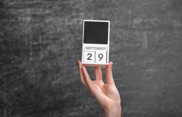 Wooden block calendar with date september 29 in female hand on background of school chalk blackboard