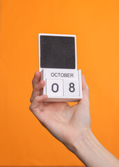 Wooden block calendar with date october 08 in female hand on orange background