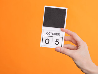 Wooden block calendar with date october 05 in female hand on orange background