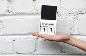 Woman's hand holds wooden block calendar with date november 11 on brick wall background