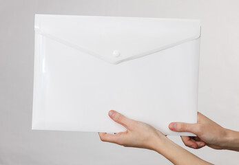 Female hand holding a white plastic folder on gray background