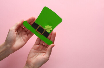Female hands hold a leprechaun hat made of paper on a pink background. Hand made. St. Patrick's Day