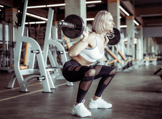 Athletic beautiful woman squats with barbell on her shoulders in the gym. Healthy lifestyle