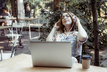 Young pretty woman with laptop listen music in headphones at outdoor coworking space