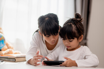 Concept kids and gadgets. Two little girls siblings sisters look at the phone and smile. They hold...