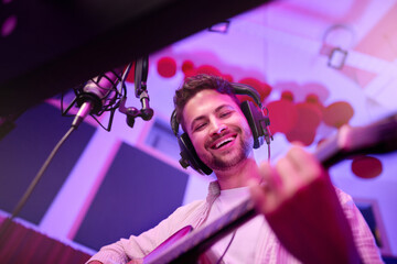 Happy man, musician or guitar in neon studio, recording production or performance for radio, label...