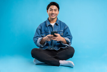 Young asian man sitting and using phone on a blue background