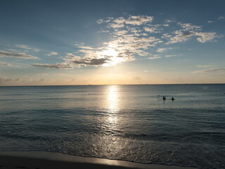 Amanecer en una playa del caribe con mar tranquilo, sol saliendo y gente empezando a caminar.