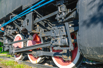 An old rusting steam locomotive is standing on a siding. Wheels and drive of an old steel locomotive. An old black steam locomotive is standing on the rails.