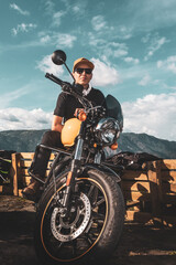 Fototapeta na wymiar caucasian boy with sun glasses on yellow motorcycle with sunset sky in the background