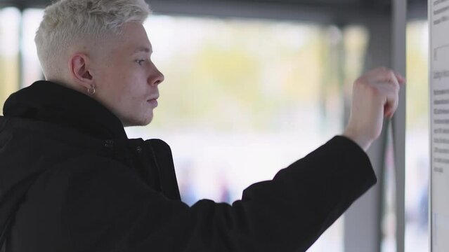 Male passenger analyzes transport card at a public transportation stop. Checking map and waiting for transport in city. Public transport route