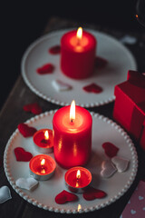 Saint Valentine's Day celebration. Red burning candles, hearts, gift box, postcard on dark wooden background. Happy holiday . Table decor for festive dinner, romantic atmosphere