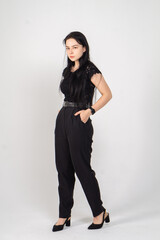 Young brunette posing standing on a white background / The model is dressed in a black jacket and trousers, there is a lot of free space around her for advertising