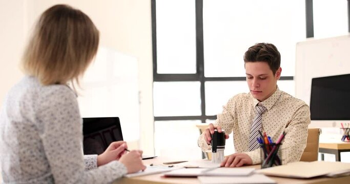 Businessman manager stamping questionnaire working with female visitor in agency office