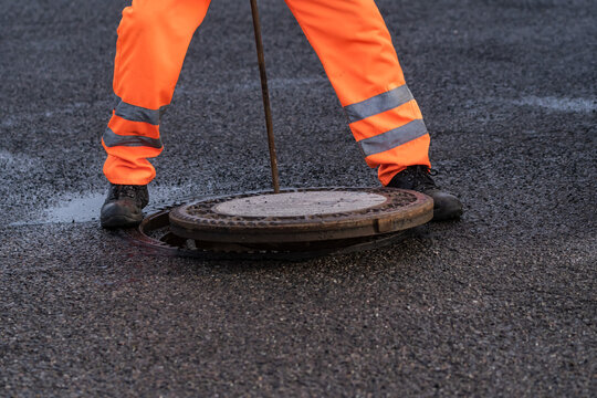Ein Arbeiter mit einer Stange verschlie&szlig;t einen Gulli mit einem Gullideckel