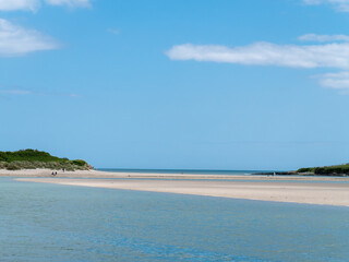 Clear sky over a beautiful sandy beach. A few people on a sandy beach. Picturesque seascape of Ireland on a summer day. A copy space. People walking on beach