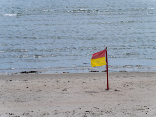 Red and yellow flag allowing swimming on the sandy seashore. Public beach.