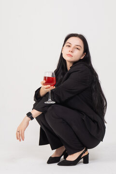 Cute young brunette girl with a glass of wine on a white background. Image of an alcoholic woman who squats