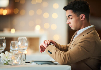 Time check, watch and late date of a man at a restaurant table on valentines day alone. Bokeh lights, night and suit of a person waiting for dinner and looking at his smartwatch on anniversary