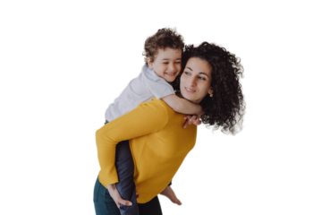 Young smiley curly woman having fun with son, rolls him on back smiling wide. Babysitter in yellow sweater, green pants entertains little cheerful child against transparent background. sister, brother
