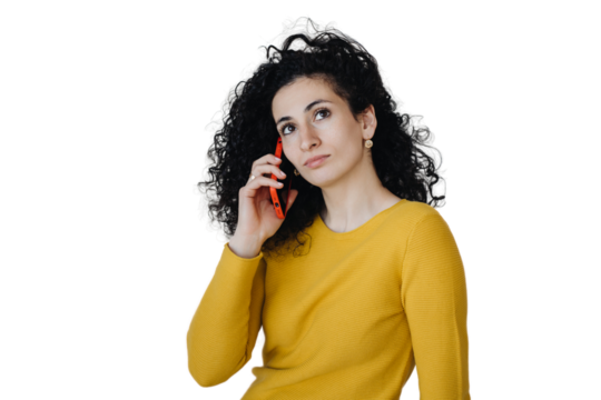 Curly Spanish young woman in yellow sweater talking by phone remote working against transparent background. Purposeful hispanic female entrepreneur speaking with business partner. Caucasian housewife