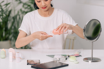 smiling young woman applying lotion to cotton disc for washing her face