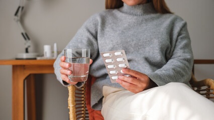 Closeup image of a woman holding pills blister pack and a glass of water