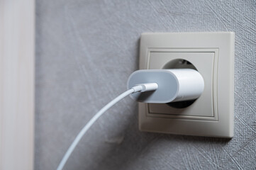 Horizontal photo. Phone charger in an electrical socket on the wall, close-up