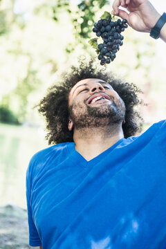 Man with bunch of grape at lakeshore in the English Garden, Munich, Germany