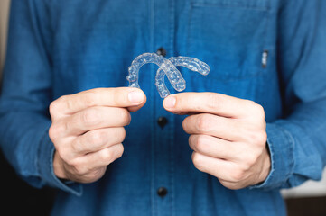 close-up of a young man, holding an invisible tooth alignment retainer in his hands. beautiful...