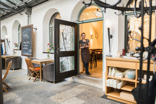 Interior of café with owner holding tablet and leaning by door