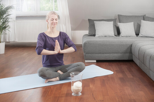 Young woman doing lotus pose yoga on exercise mat in living room, Bavaria, Germany