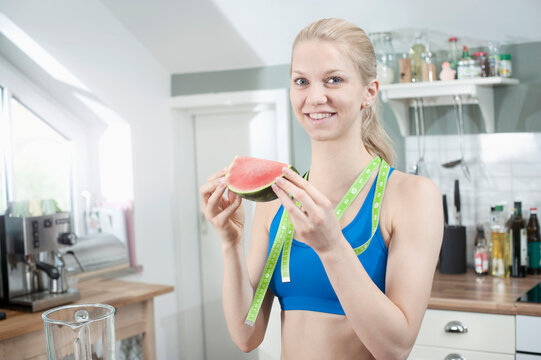 Young woman eating slice of watermelon in the kitchen, Bavaria, Germany