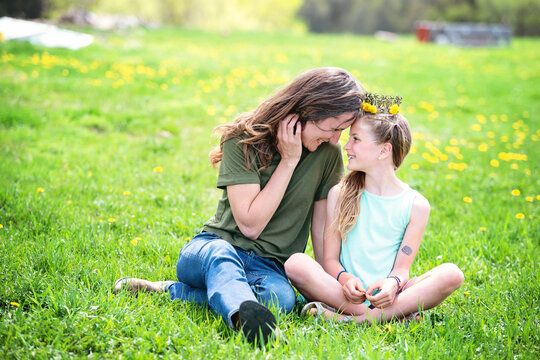 Mother and tween daughter sitting in a dandelion meadow.