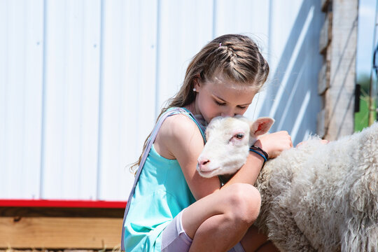 Blond tween girl hugging a lamb.