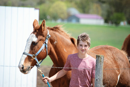 Blond tween boy leading a brown horse with white blaze.