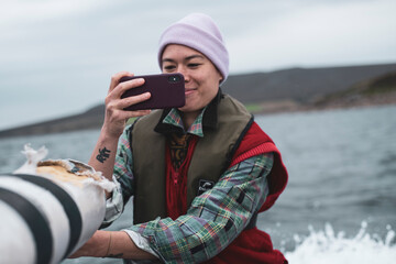 Asian person takes photo with phone on back of boat in Scotland