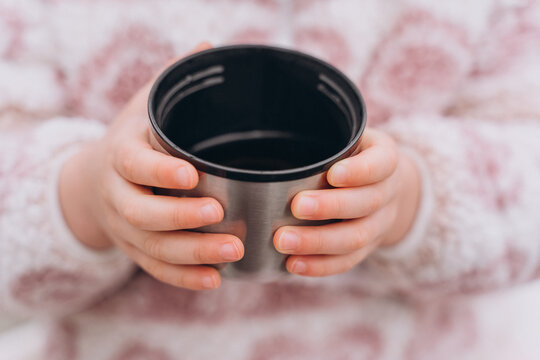 Baby girl in light pink warm clothes drinks tea from a thermos