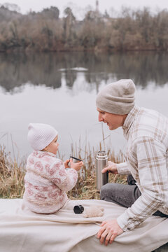 Dad and baby daughter are sitting by the river and drinking tea 