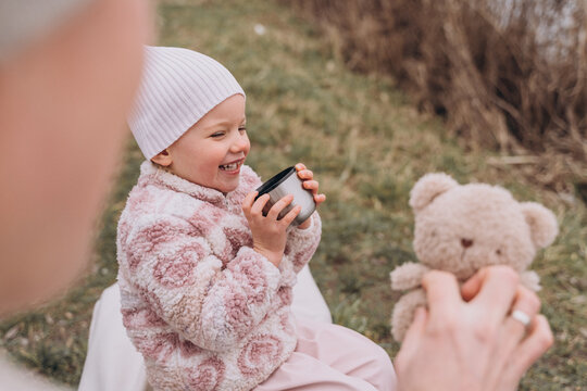 Toothless baby girl in the park laughs and drinks tea from the thermos