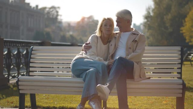 Happy lovely caucasian senior couple sitting in bench and hugging each other. Realtime