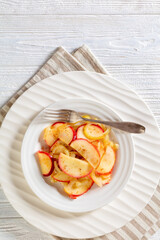 fried onion and red apple slices on white plate with fork on white wood table, vertical view