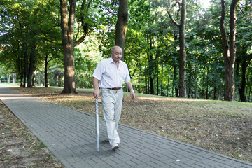 An old, stooped man walks sullenly and alone along the path in the park with a gray umbrella instead of a cane.
