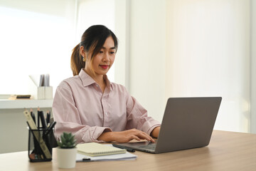 Concentrate asian female office worker analyzing financial data on laptop and making notes on notebook
