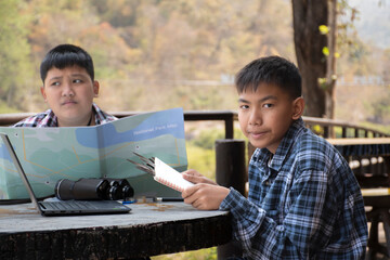 Asian boys are at the local national park, they are consulting, talking, doing their school project...