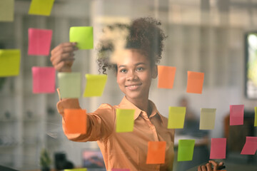 Confident African American female manager analyzing process schedule, planning tasks on sticky...