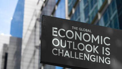 The global economic outlook is challenging on a black city-center sign in front of a modern office...