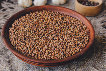 Raw buckwheat grains in a clay bowl on a linen bedding. Rustic background.